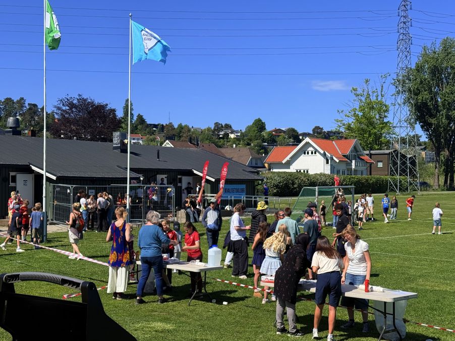 En gruppe mennesker som står på en plen med et flagg og en bygning i bakgrunnen