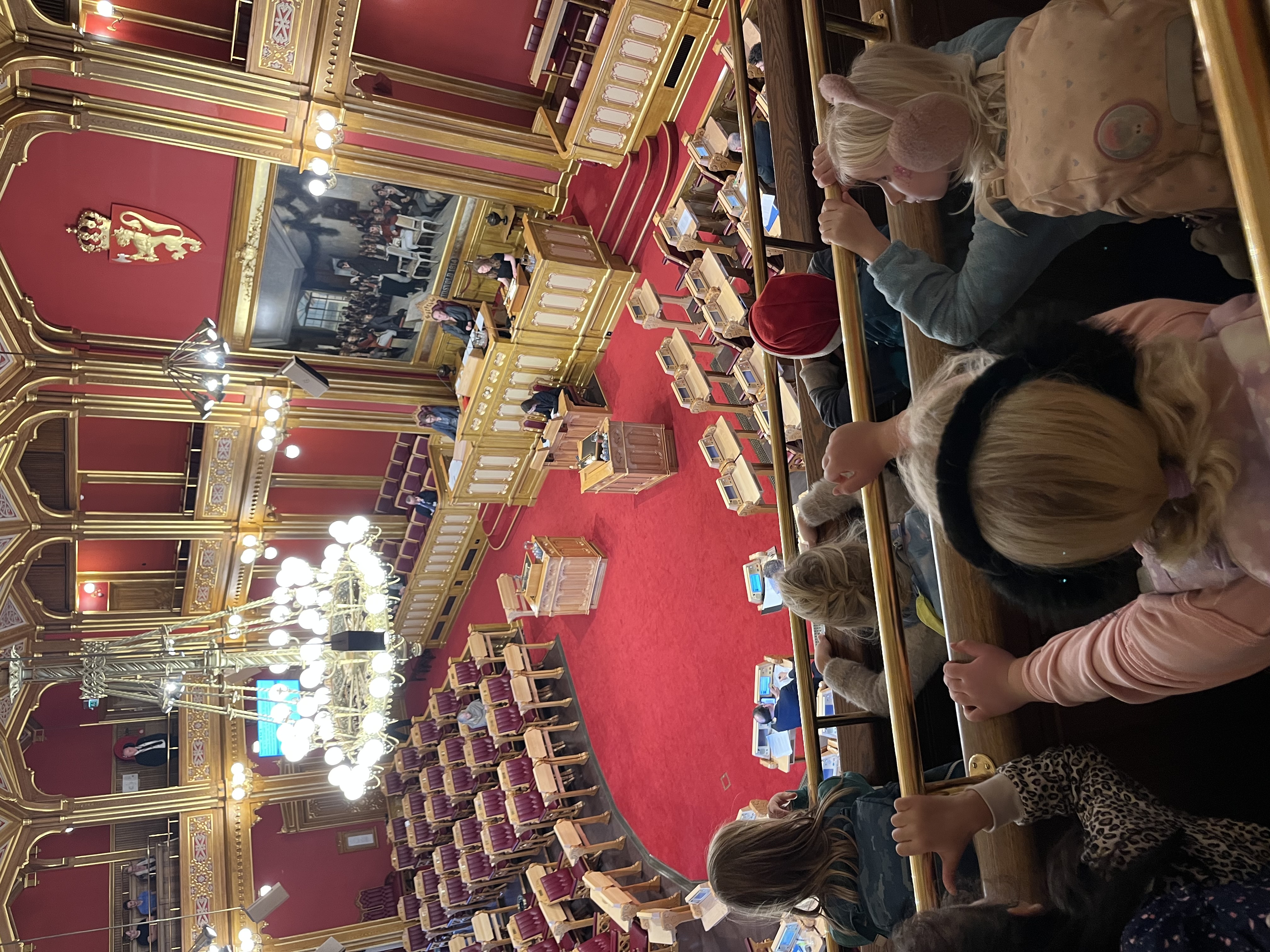 en gruppe mennesker som sitter i et rom med en scene og en stor rød løper