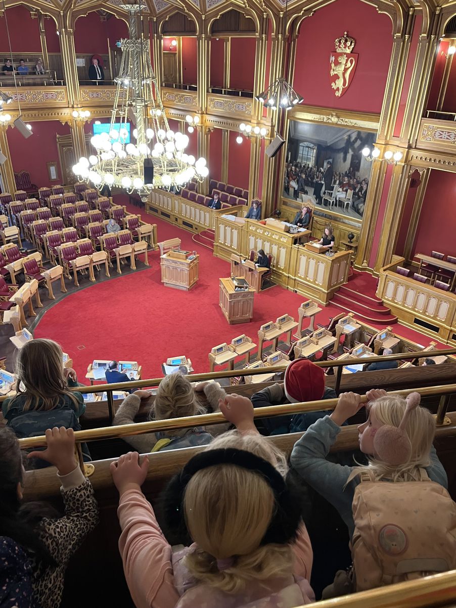 en gruppe mennesker som sitter i et rom med en scene og en stor rød løper